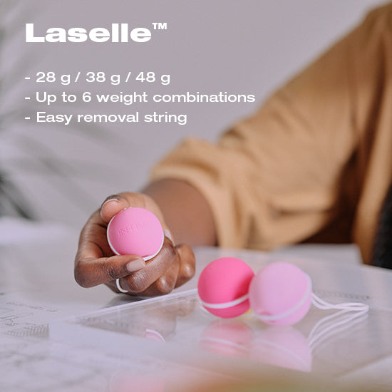 Hand holding INTIMINA LASALLE Kegel ball with two other pink balls on tabletop