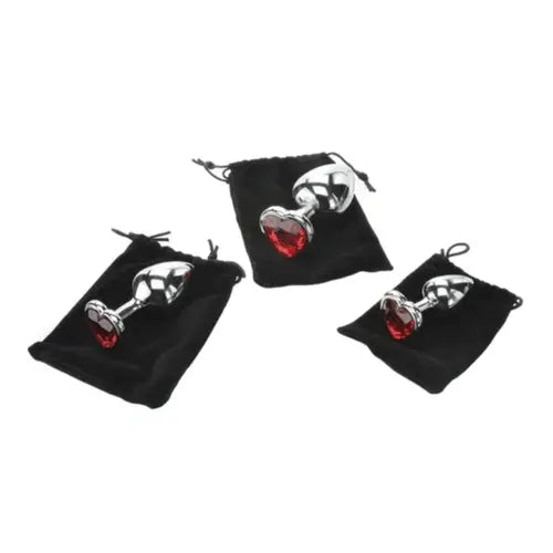 set of three metal butt plugs with red heart gem base on black velvet storage bags against white background