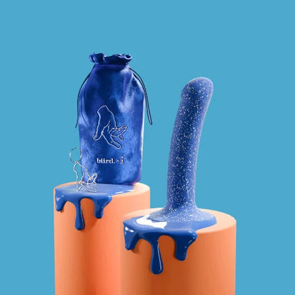 blue dildo with white speckles on orange pedestal next to blue storage bag