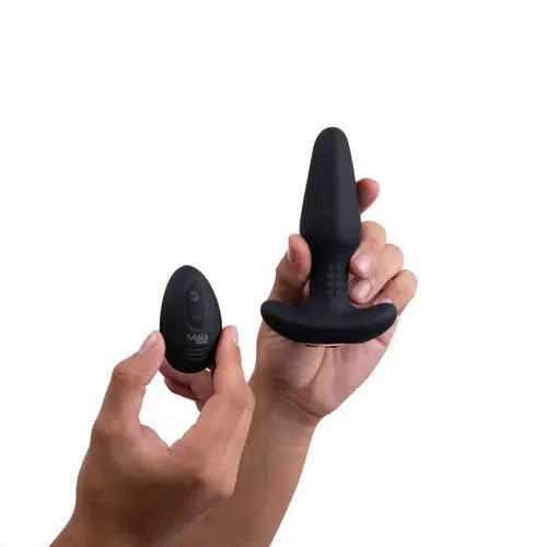 Hands holding Black Devin Butt Plug and black remote control against white background