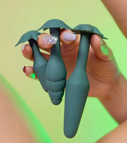 Hand with sparkly nails holding the DOOBIE anal trainer kit - 3 dark green anal plugs in small, medium, and large