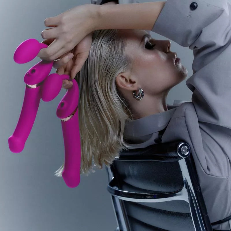 woman holding two strapless fuchsia strap-ons behind her head